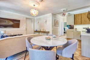A modern dining area with a marble table, grey upholstered chairs, and a decorative chandelier.
