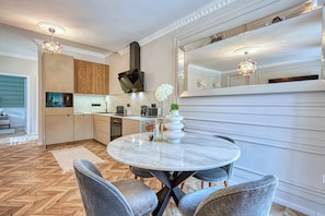 A modern kitchen with built-in appliances, a round marble dining table, and grey upholstered chairs.