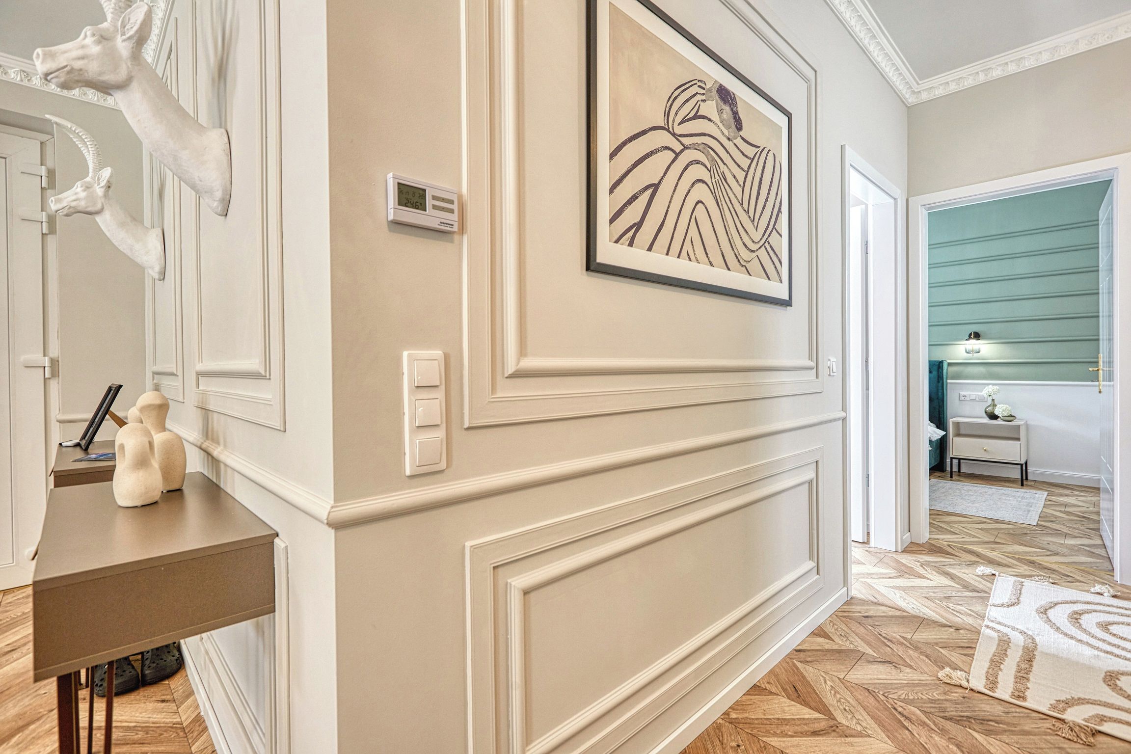 A hallway with a marble wall, a framed artwork, a thermostat, and a door leading to another room.