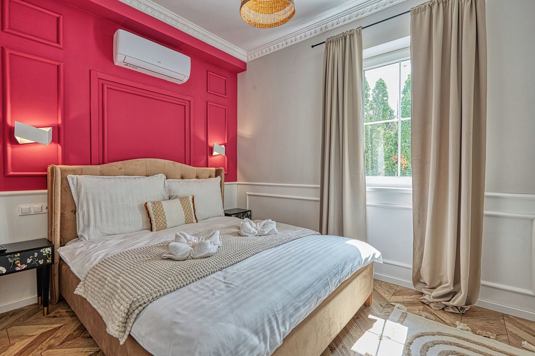 A hotel room with a bed, a nightstand, a window with curtains, and a wall-mounted air conditioner.