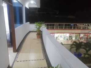 Un balcón con suelo de baldosas, plantas en macetas y vistas a una zona comercial que incluye una tienda Sony.