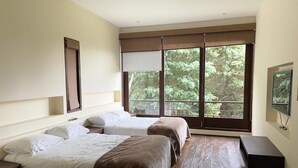 A hotel room with two beds, a large window with a view of trees, a flat-screen TV, and a wooden floor. - Rest house in Yerbabuena (Sopo)