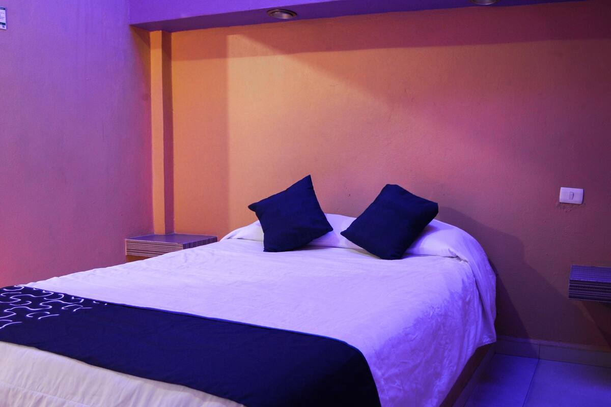 Un lit bien fait, recouvert d’une couverture blanche et bleu foncé, avec deux oreillers bleu foncé et un plaid bleu foncé.