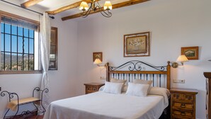 Ein Schlafzimmer mit einem großen Bett, einem Holzkopfteil, zwei Nachttischen, einer Bank und einem Fenster mit Blick.