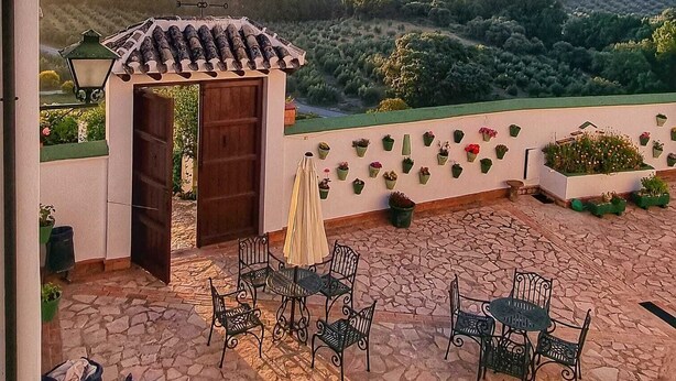 Eine Terrasse mit Sitzgelegenheiten, einem Zierbogen und Blick auf ferne Hügel.