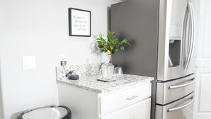 Een moderne keuken met een roestvrijstalen koelkast, een marmeren aanrechtblad, een vuilnisbak en een geïnspireerd citaat in een lijst op de muur.