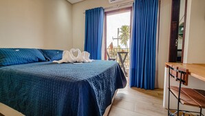 A bedroom with a bed, a wooden desk, and a balcony with blue curtains. - Sete Mares (Maragogi)