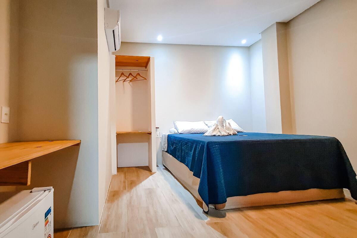 Une petite chambre bien éclairée, avec un lit simple, un bureau en bois et une armoire.