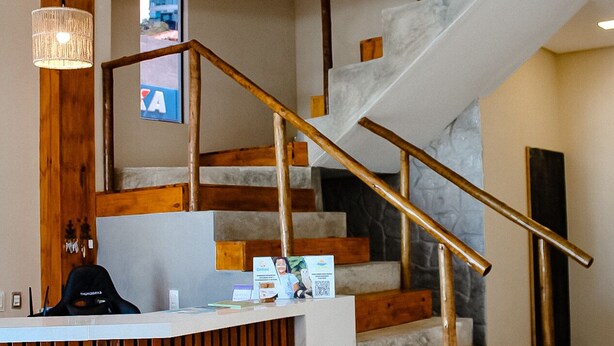 A modern reception area with a wooden desk, a staircase with wooden railings, and two hanging light fixtures. - Sete Mares (Maragogi)