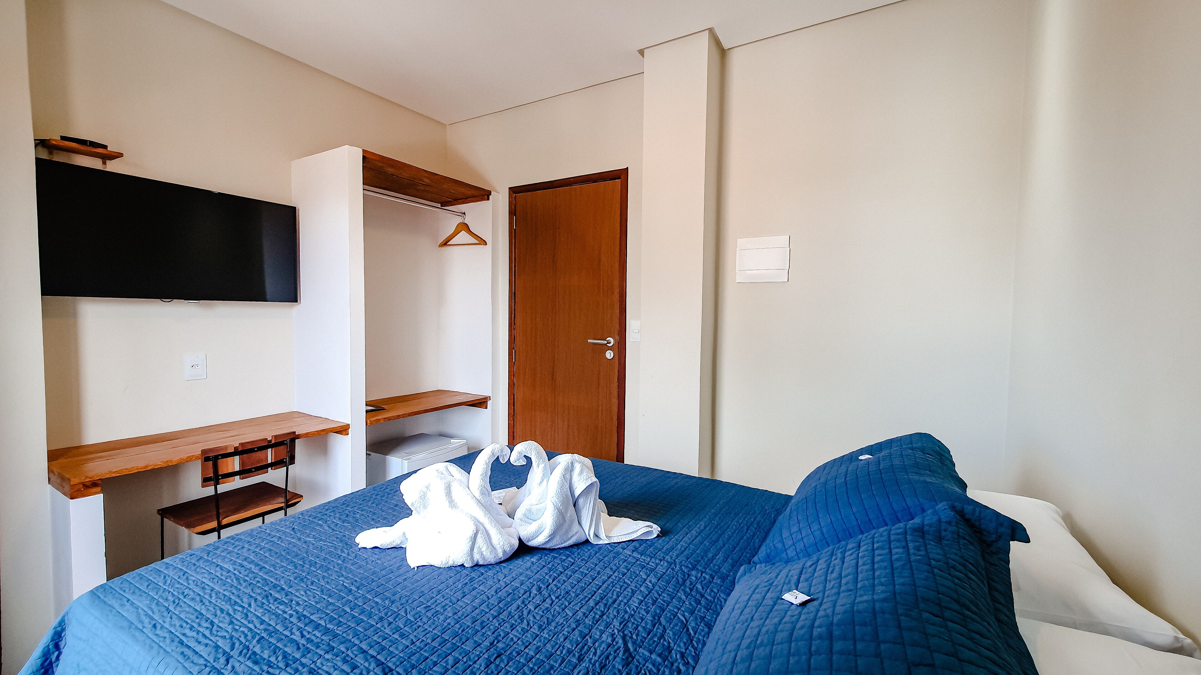 Un dormitorio con una cama, televisión montada en la pared, un banco de madera y un armario.
