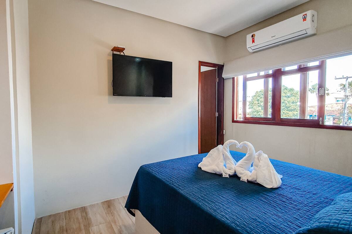 Une chambre dotée d’un lit, d’un téléviseur à écran plat fixé au mur, d’un appareil de climatisation et d’une fenêtre donnant sur l’extérieur.