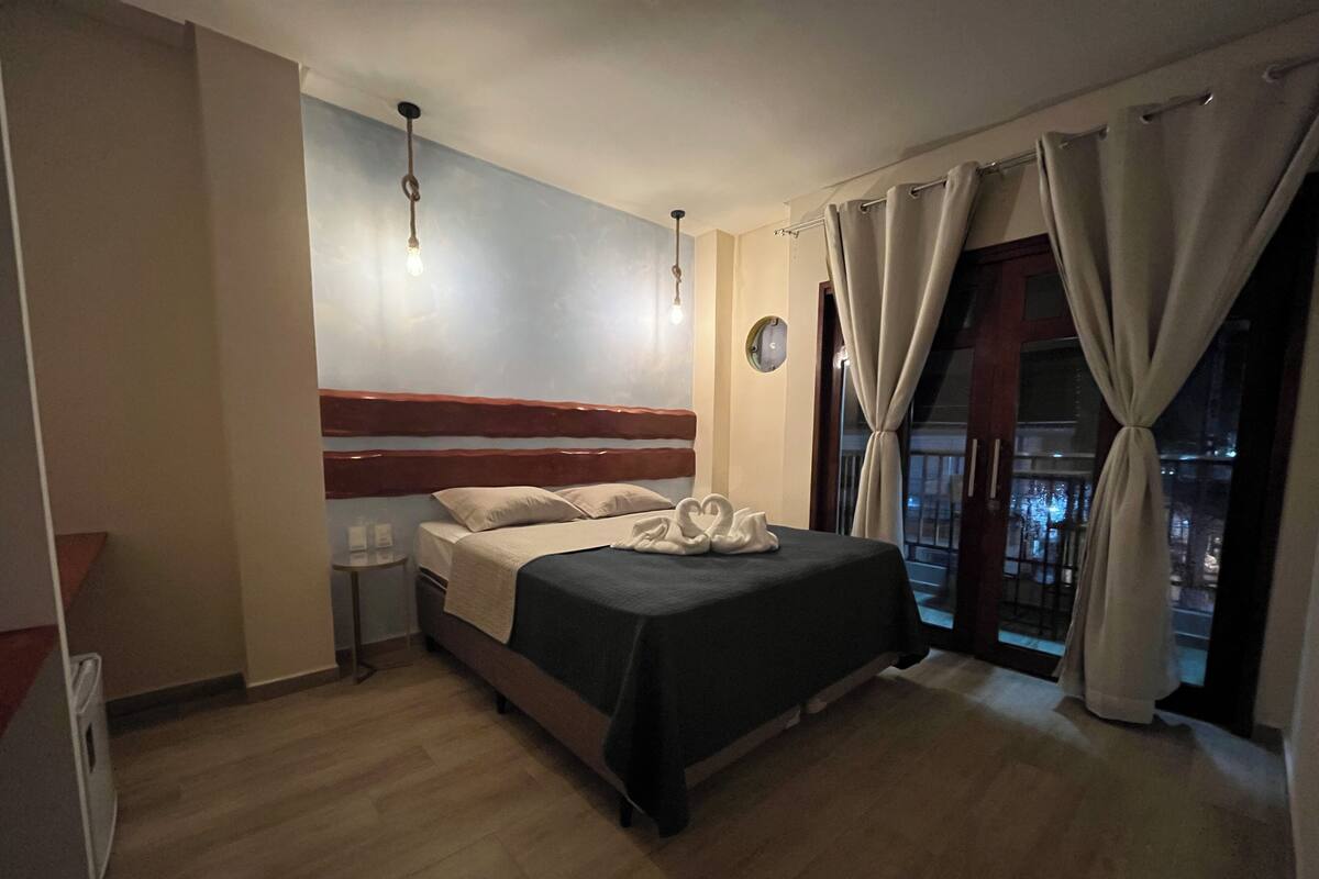Une chambre d’hôtel avec un lit, une table de chevet, une horloge murale et une fenêtre avec des rideaux.