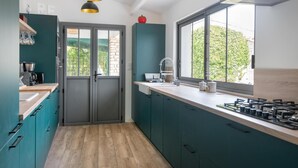 A modern kitchen with teal cabinetry, a large window, and a built-in stove. - MA RÉ HOTES        . (Le Bois-Plage-en-Ré)