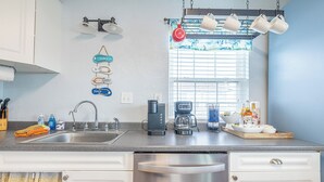 A kitchen with a stainless steel dishwasher, a coffee maker, and a window with blinds. - Pet Friendly - Walk to the Beach, Cozy Home (Freeport)