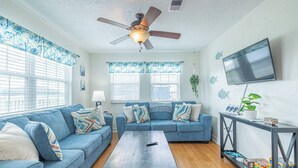 A living room with a ceiling fan, two sofas, a coffee table, and a TV on a wall. - Pet Friendly - Walk to the Beach, Cozy Home (Freeport)
