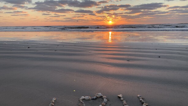 A beach with the sun setting over the horizon, and a heart made of stones on the sand. - Pet Friendly - Walk to the Beach, Cozy Home (Freeport)