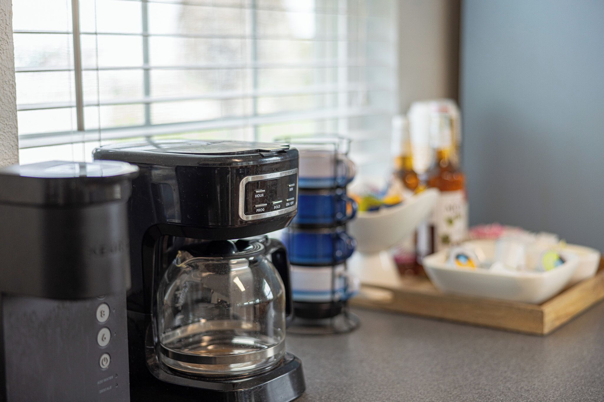 A coffee maker on a kitchen counter with a window in the background.