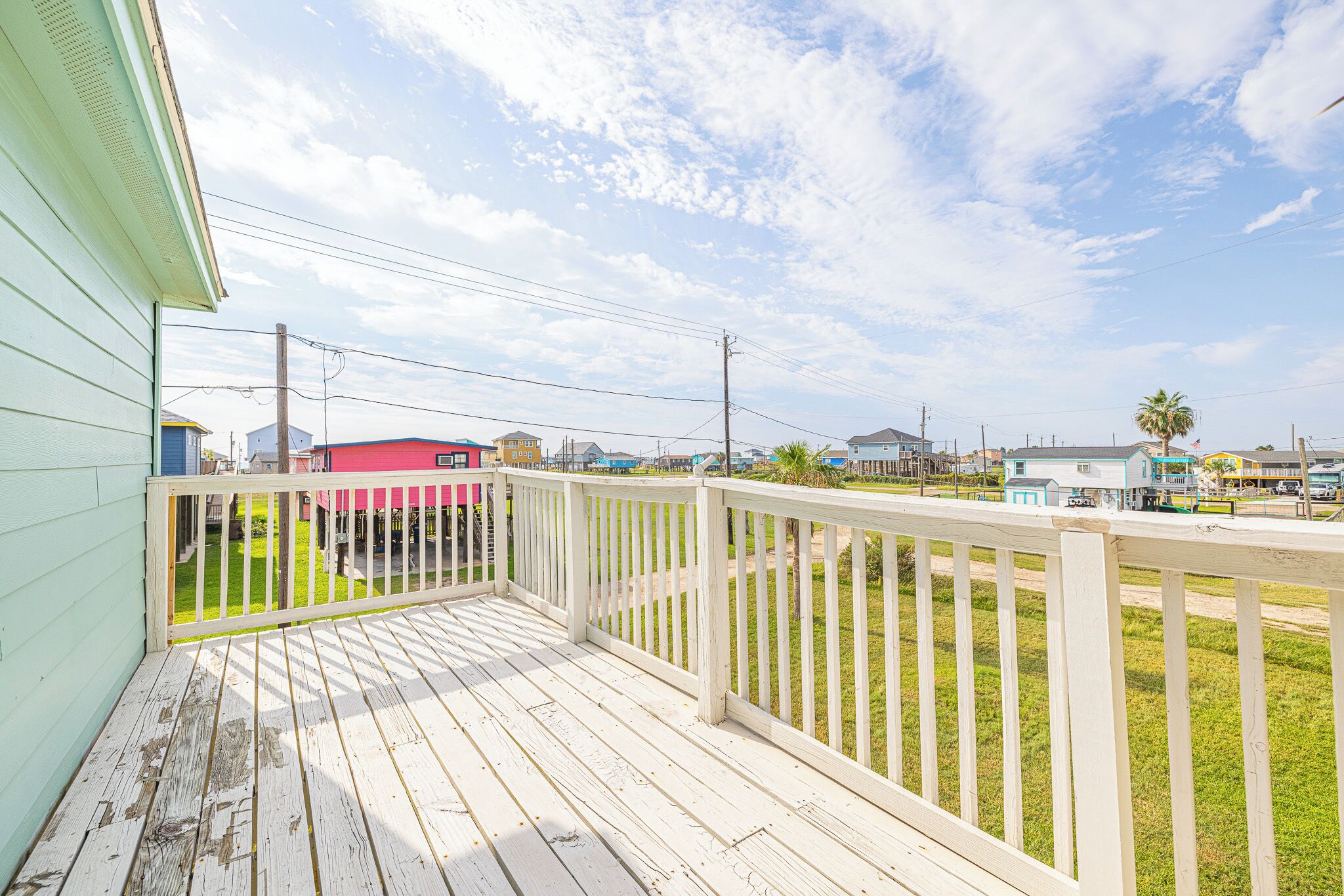 A wooden deck with a white railing, overlooking a residential area with houses and a clear sky.