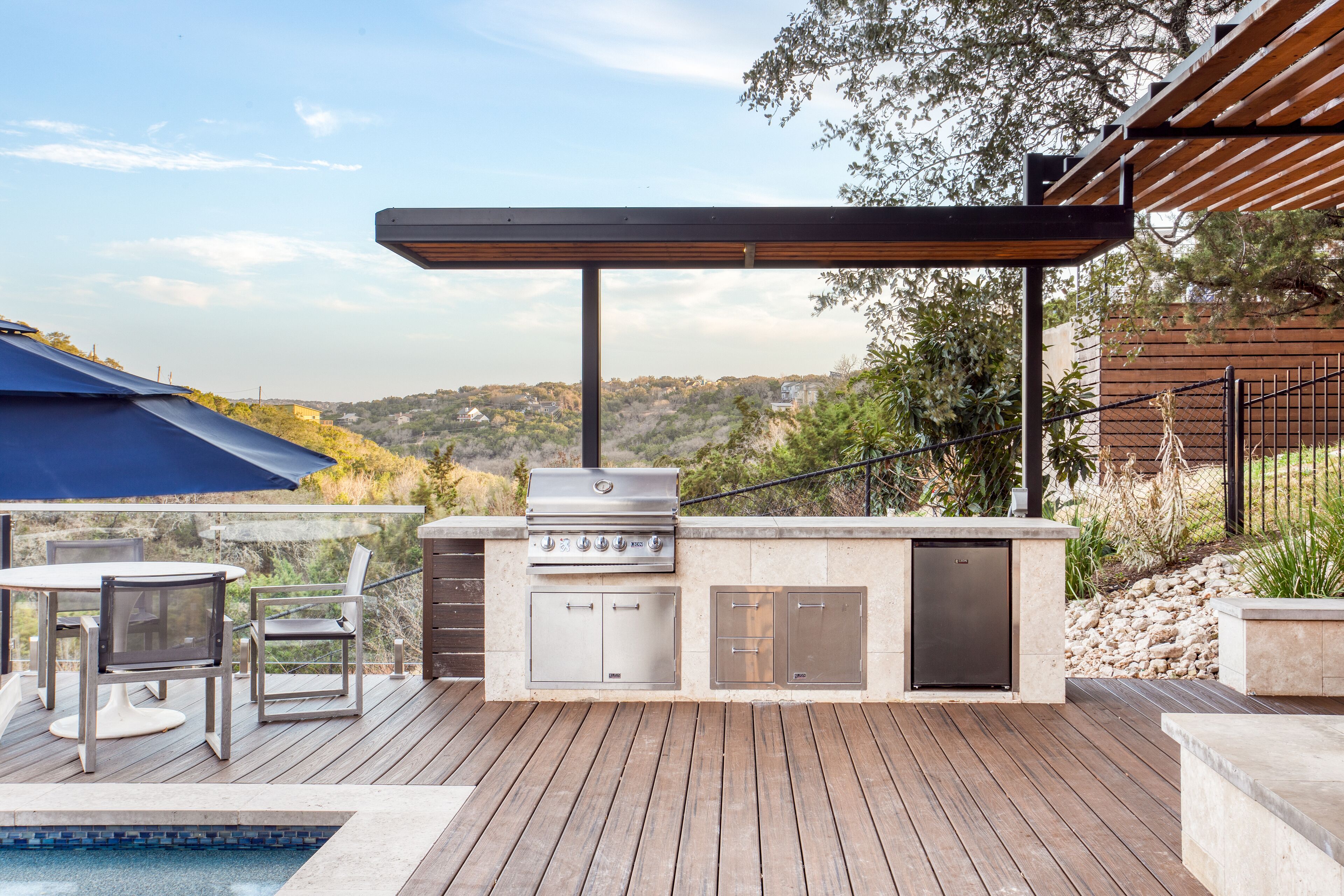 An outdoor kitchen with a grill, built-in cabinets, and a pergola.