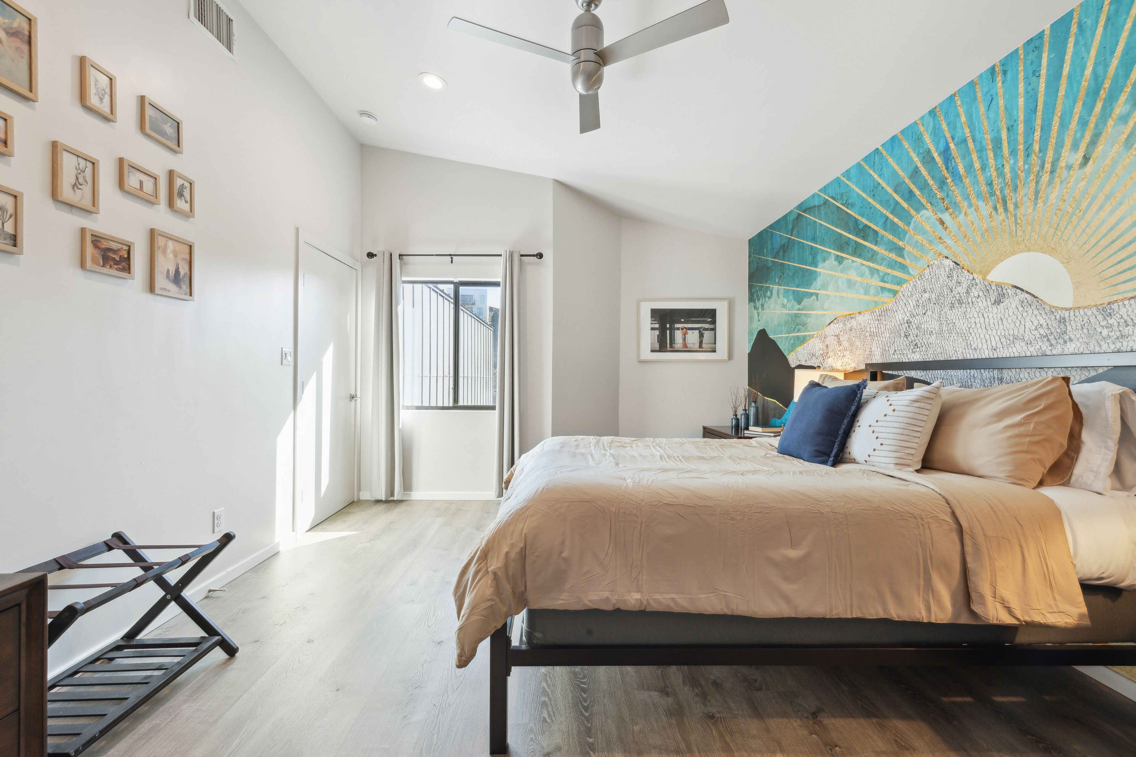 Une chambre à coucher avec un lit, un ventilateur de plafond, un mur orné de tableaux encadrés et une grande fenêtre.