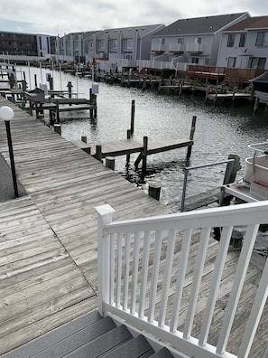 A wooden dock leading to a marina with boats, connected to a row of residential buildings.
