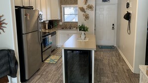 A modern kitchen with stainless steel appliances, white cabinets, a central island, and decorative wall art. - 1st floor condo mid town just a short walk to many fun things to do! (Ocean City)