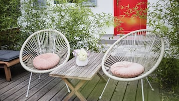 Deux fauteuils en osier avec des coussins, une table en bois et un vase rempli de fleurs.