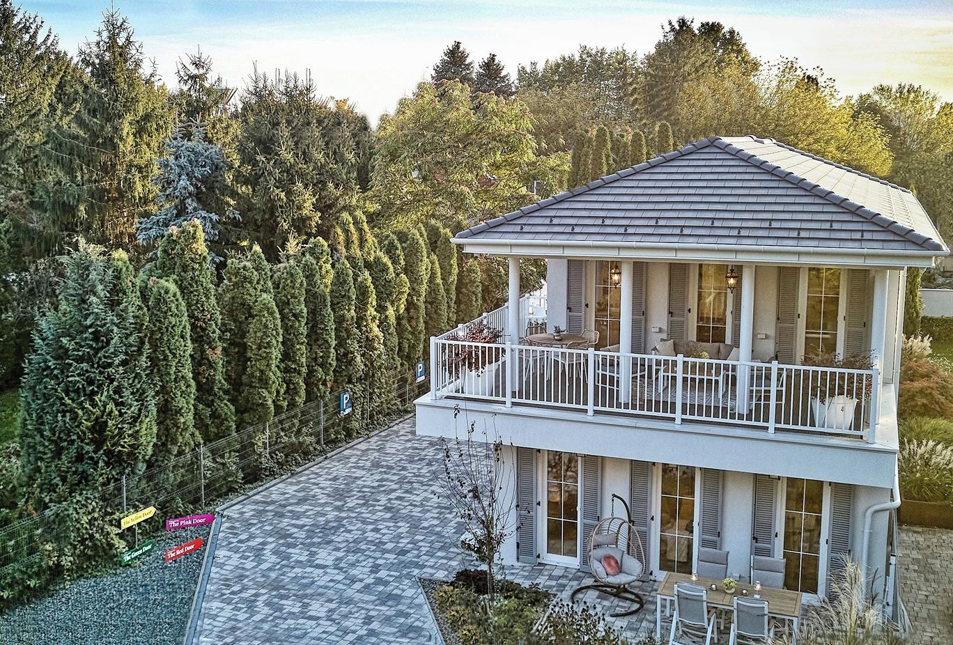 A two-story house with a balcony, surrounded by trees.