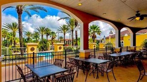 An outdoor dining area with tables and chairs, a pool, and palm trees. -  Modern townhome  Spa / Water Park resort Regal Palms minutes to Disney (Davenport)
