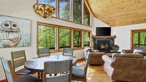 A spacious living room with a fireplace, large windows, and a painting of an owl. - CreekFront Cabin- 4 Acres- FirePit & Place- Game Tables- Private Yet Close to BR (Mineral Bluff)