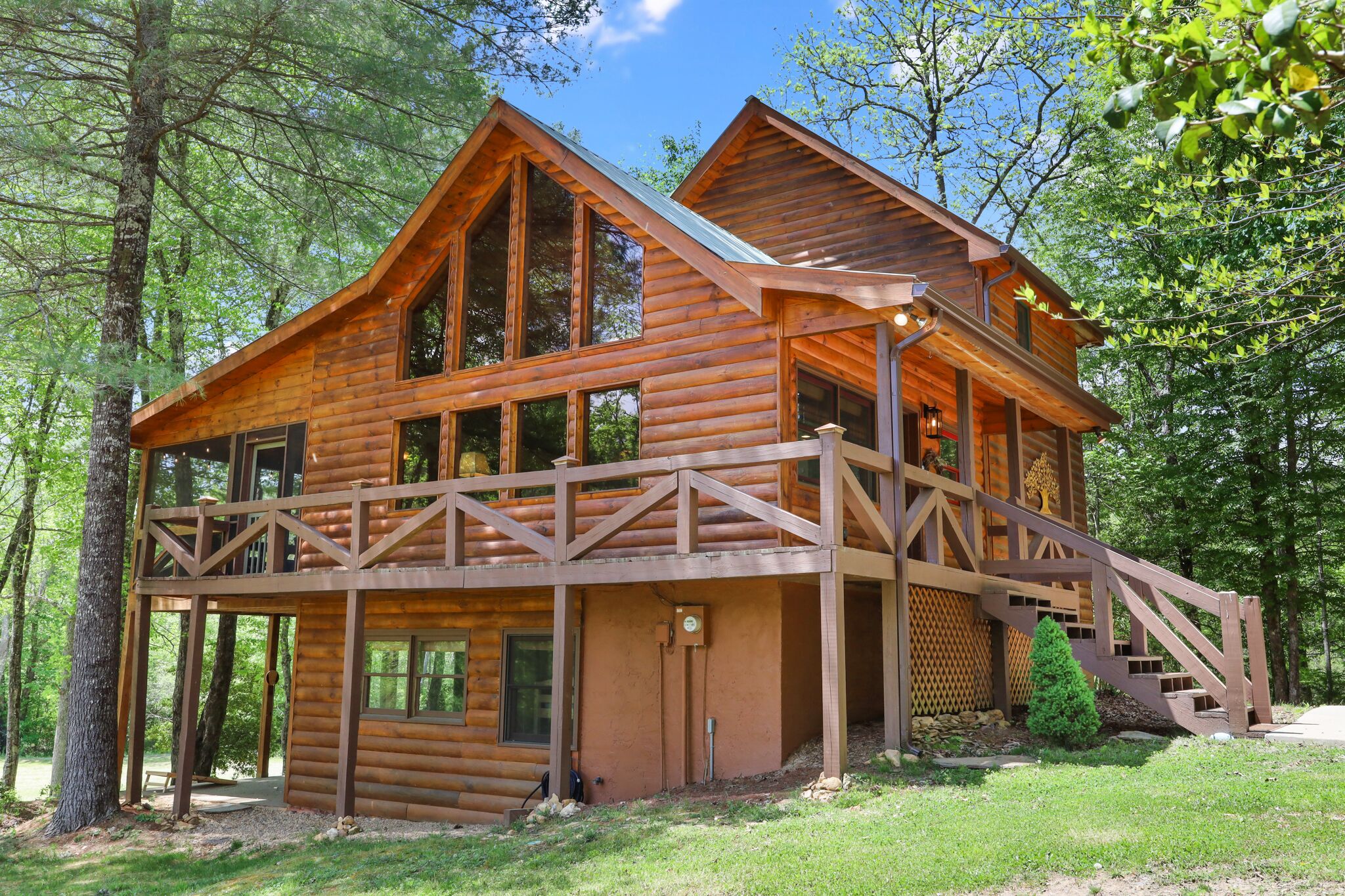 A wooden cabin with a balcony, large windows, and a staircase leading to the upper level.