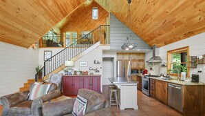 A spacious living area with a high ceiling, wooden floors, a kitchen with modern appliances, and a staircase leading to an upper level. - CreekFront Cabin- 4 Acres- FirePit & Place- Game Tables- Private Yet Close to BR (Mineral Bluff)