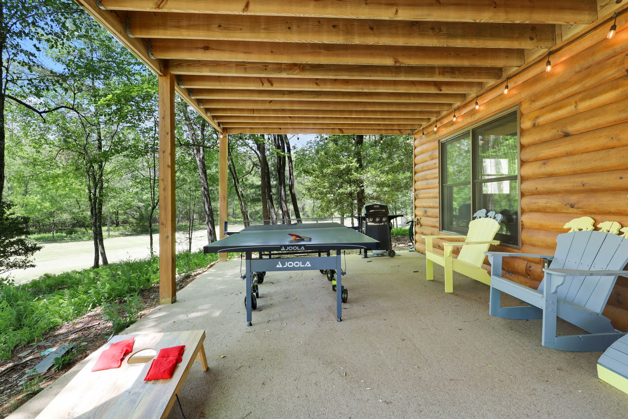 A wooden deck with a pool table, Adirondack chairs, and a barbecue grill.