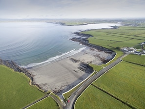 Luchtbeeld van een kustgebied met een strand, landbouwgrond en een weg die langs de kust slingert.