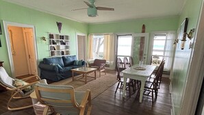 A spacious living room with a dining area, wooden flooring, and a ceiling fan. - Original Torch Lake Cottage from 1910 (Alden)