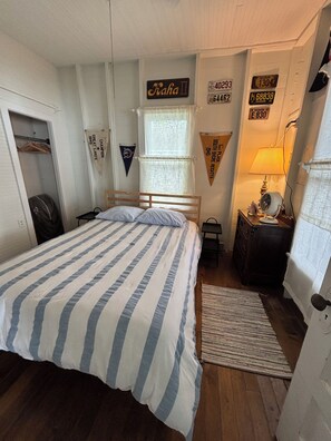 Un dormitorio con cama, tocador, lámpara y diversas decoraciones en la pared, incluyendo placas de automóvil y banderines.