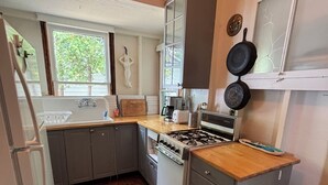 A compact kitchen with a stove, oven, and a window providing natural light. - Original Torch Lake Cottage from 1910 (Alden)