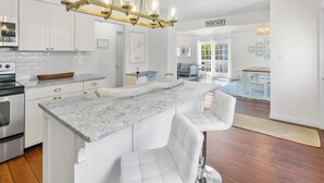 Una cocina moderna con armarios blancos, encimera de mármol y una isla central con taburetes de bar.