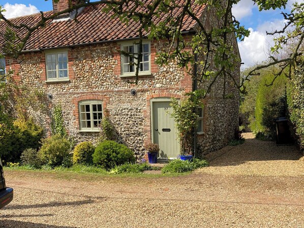A stone house with a red-tiled roof, a green door, and a gravel driveway.