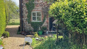 Une maison de campagne en pierre, dotée d’une fenêtre, entourée d’un jardin planté et agrémentée d’un abreuvoir à oiseaux.