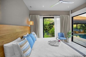 Et hotelværelse med en stor seng, en loftsvifte, udsigt til en swimmingpool og en skydedør til terrassen.