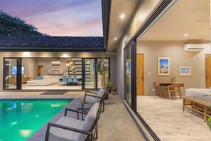 A modern outdoor living area with a pool, seating, and a view of the interior.
