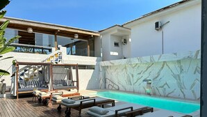 A modern outdoor pool area with wooden loungers and a stone wall. - Santorini Beach Hotel (Porto Seguro)