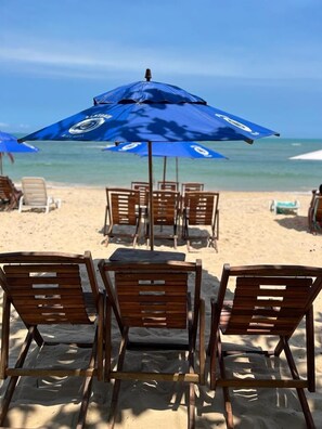 Na praia, areia branca, barracas de praia de cortesia, espreguiçadeiras 