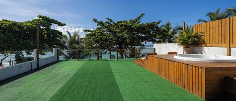 A rooftop with artificial grass, a wooden deck, and a hot tub.