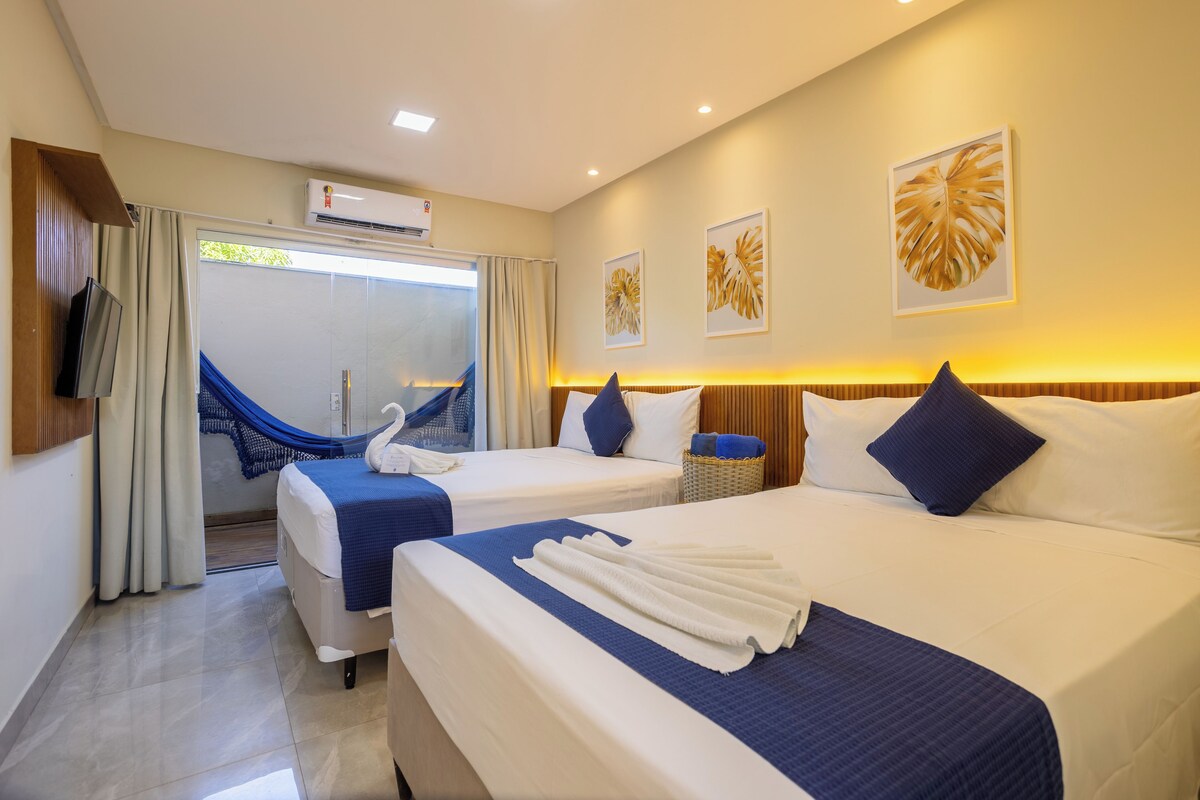 A hotel room with two beds, a TV, a hammock, and artwork on the walls.