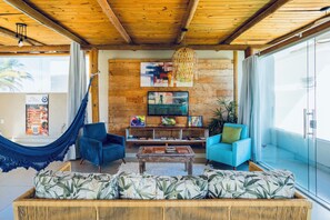A modern living room with a hammock, blue sofas, a wooden coffee table, and artwork on the wall. - Santorini Beach Hotel (Porto Seguro)