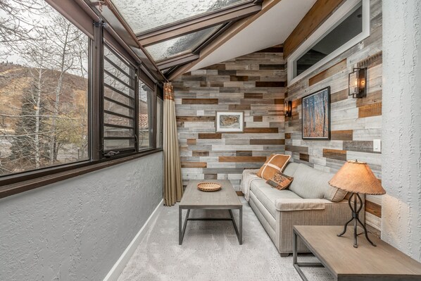 Una habitación con un ventanal grande, pared de madera, sofá, mesa y una lámpara.