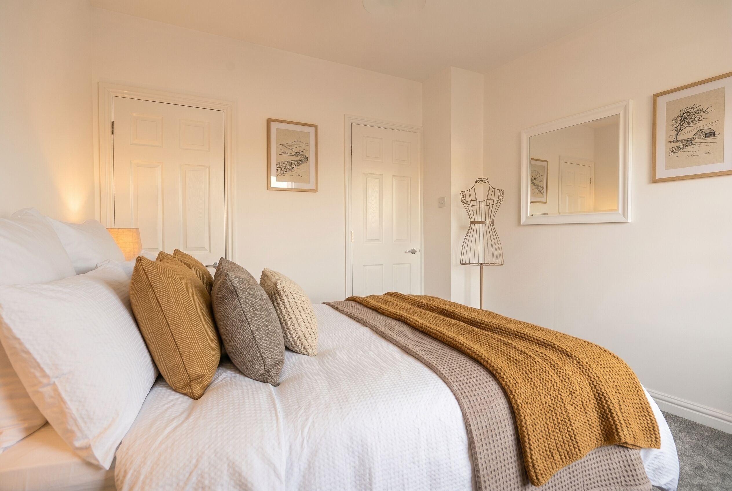 A neatly made bed with pillows and a blanket, a door, and two framed pictures on the wall.