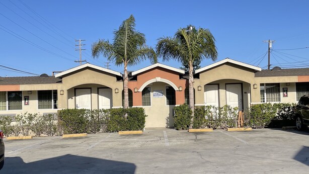 A motel with a central archway, parking lot, and palm trees. - Villa Inn & Suites (Inglewood)